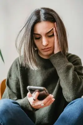 una mujer dudando con aspecto triste o agobiada por algo, sostiene el teléfono en la mano